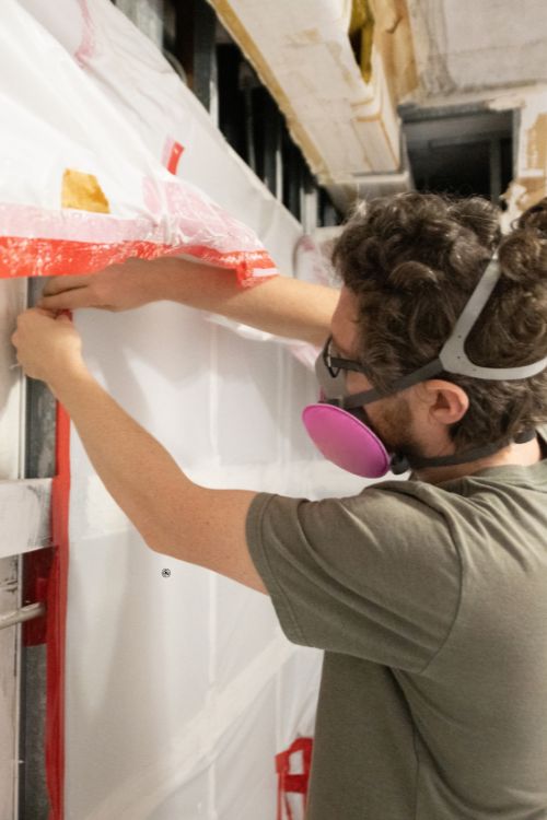 A man wearing protective gear works on a wall during a mold removal service in Jacksonville, FL.