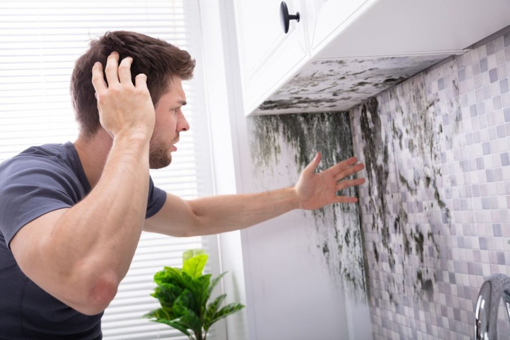 A man stands in front of a sink covered in mold, highlighting a potential cleanliness issue in the environment.